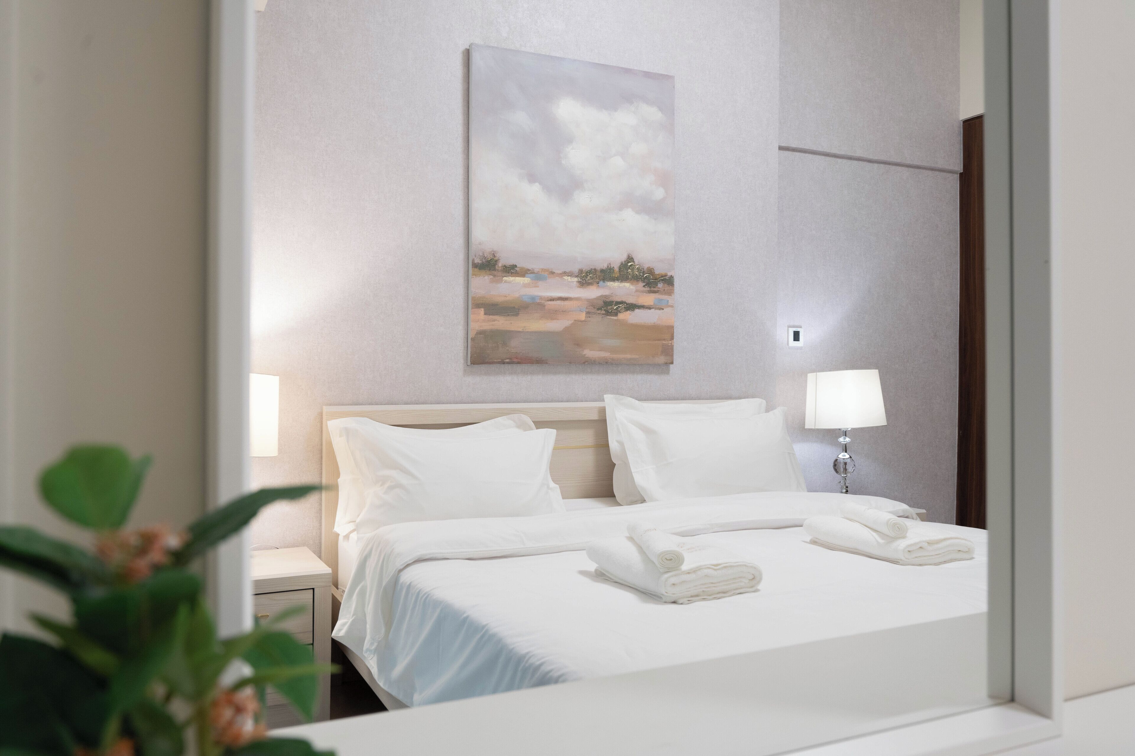 Une chambre d’hôtel avec un lit, du linge de lit blanc, un tableau au mur et une table de chevet avec une lampe.