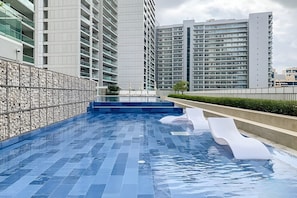 A modern swimming pool with a tiled deck, surrounded by high-rise residential buildings. - Dubai Luxury 2BR - Burj Khalifa View (Dubai)