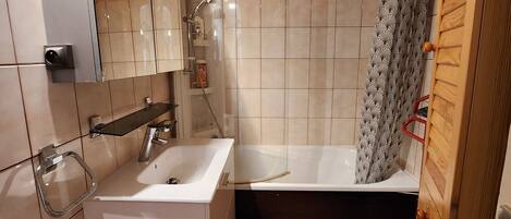A modern bathroom with a white sink, a glass shower enclosure, and a wooden door.