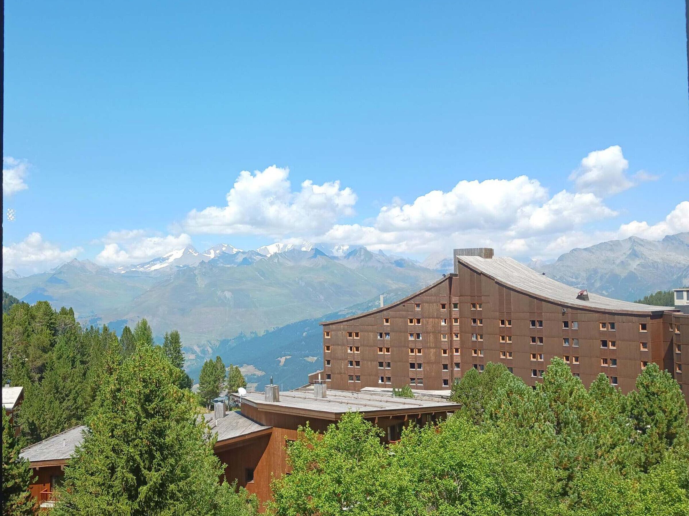 Ein Hotel mit modernem Design, das ein gewölbtes Dach und zahlreiche Fenster aufweist. Es wird von üppiger Vegetation umgeben und bietet einen Blick auf schneebedeckte Berge im Hintergrund.