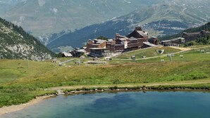 Un chalet de montagne composé de plusieurs bâtiments, avec un petit étang et des montagnes enneigées en arrière-plan.