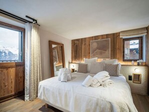 A hotel room with a large bed, wooden paneling, a view of mountains, and a window with curtains. - Modern chalet in Courchevel with sauna and jacuzzi (Courchevel 1550)