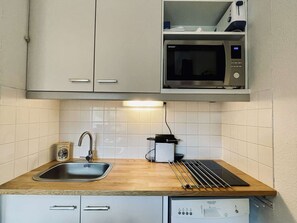 Eine kleine Küche mit Spüle, Mikrowelle und Geschirrtrockner.