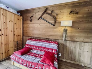 A wooden room with a bed, a wardrobe, and a wall-mounted lamp.