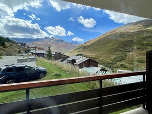 Vista desde un balcón sobre un paisaje rural con montañas, una carretera y edificios.