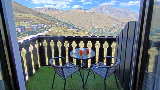 Un balcone con due sedie e un tavolo, affaccia su un paesaggio montuoso con edifici in lontananza.