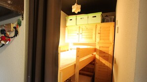 Een kleine kamer met een stapelbed, houten kasten en een hanglamp.