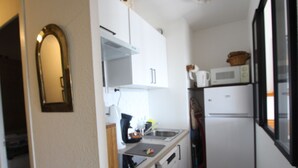 Een kleine keuken met witte kastjes, een magnetron en een koelkast.
