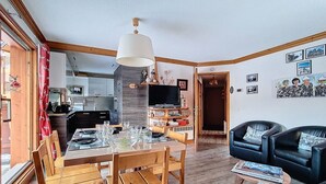 Una sala moderna con comedor, muebles de madera, un televisor y una estantería.