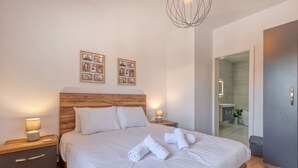 A neatly made bed with white linens and rolled towels, a wooden headboard, and two bedside tables with lamps. - Qala Tranquil Escape - Stylish With Terrace AC (Qala)