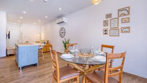 A modern dining area with a glass table, wooden chairs, and a kitchen in the background. - Qala Tranquil Escape - Stylish With Terrace AC (Qala)