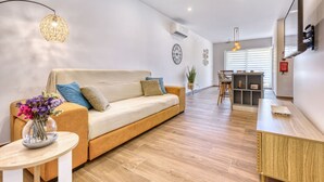 A modern living room with a sofa, a small table with a vase of flowers, a dining area with a bar counter, and a kitchen in the background. - Qala Tranquil Escape - Stylish With Terrace AC (Qala)