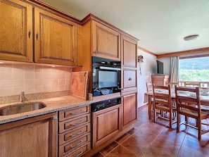 Uma cozinha com armários de madeira, forno embutido, pia e sala de jantar com mesa e cadeiras.