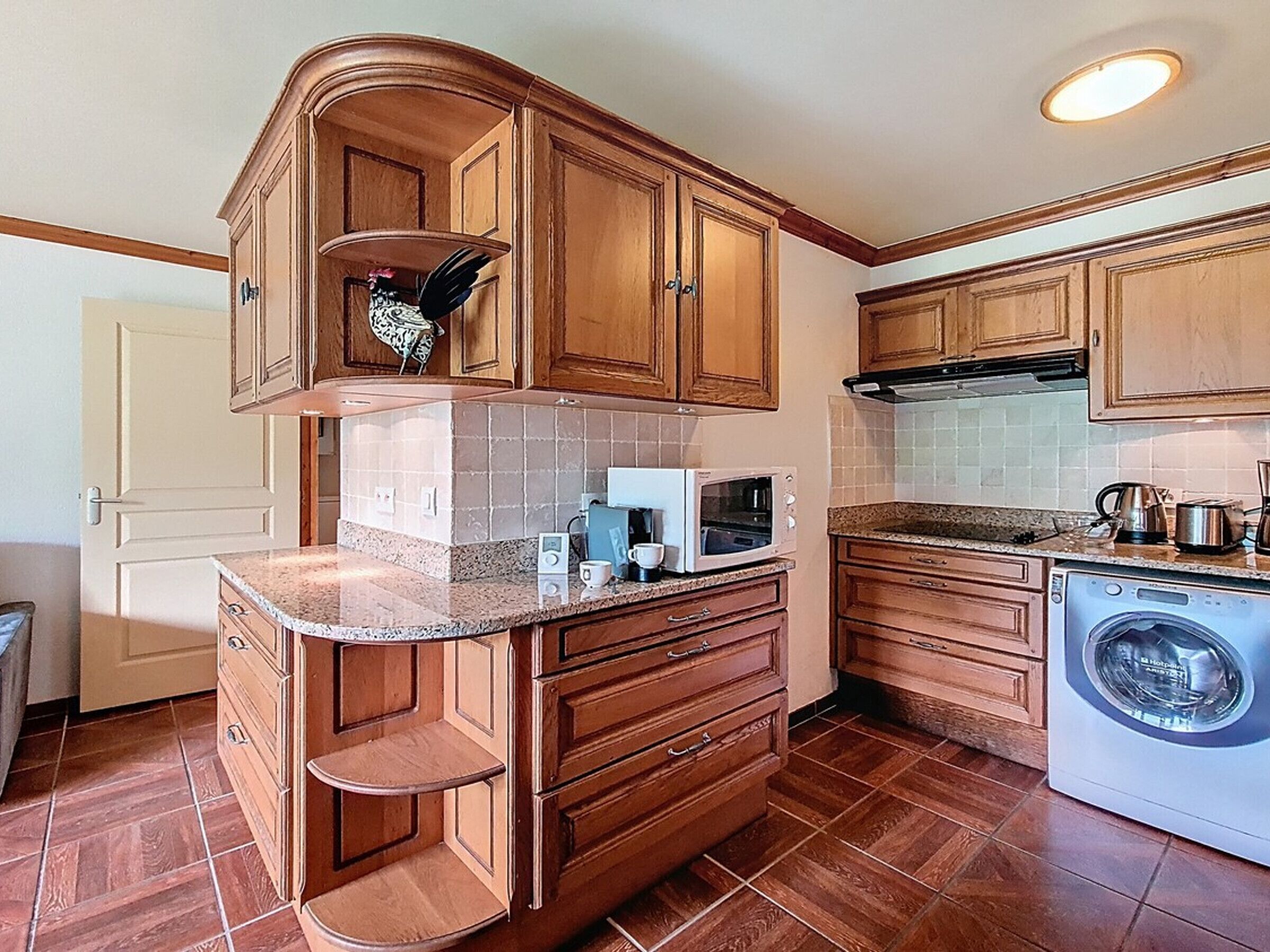 Cocina con armarios de madera, microondas integrado, lavadora y cafetera.