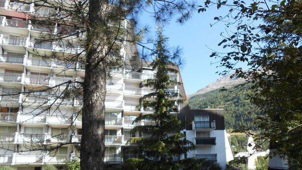 A multi-story residential building with balconies, surrounded by trees and a mountain in the background. - Bright apartment close to slopes, balcony and parking (La Salle-les-Alpes)