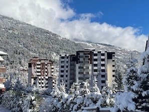 A modern building with a unique checkered facade, surrounded by snow-covered trees and a mountainous backdrop.