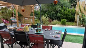 Un espace extérieur aménagé pour les repas, avec une piscine en arrière-plan.