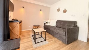 Een moderne woonkamer met een grijze bank, een houten salontafel, een klein bijzettafeltje en een tv die aan een houten kast is bevestigd.