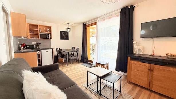 Een gezellig en compact verblijf met een bank, een eettafel, een keukenhoek en een aan de muur bevestigde televisie.