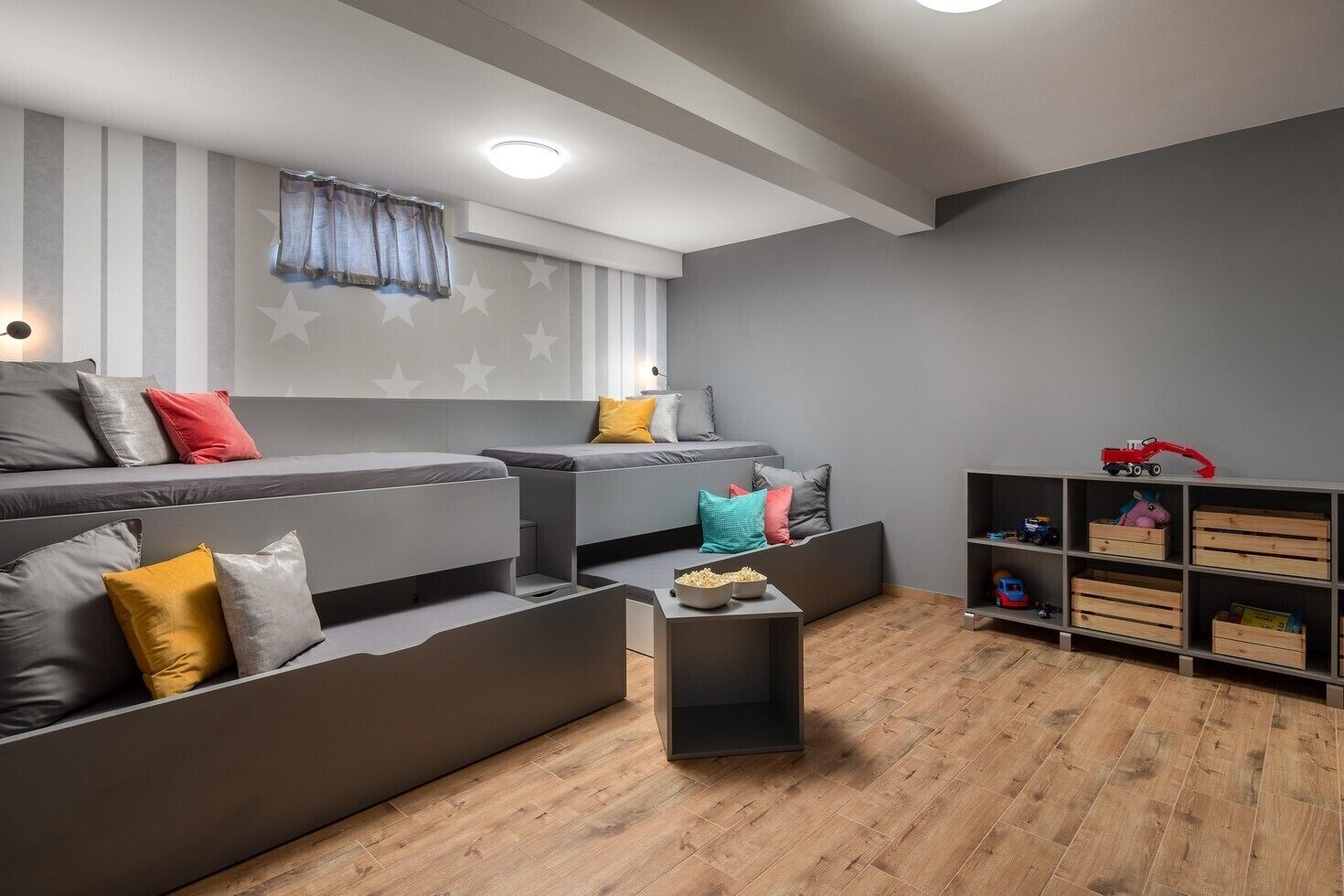 Een moderne woonkamer met een hoekbank, een bijzettafeltje met een schaal popcorn en een houten wandplank voor speelgoed.