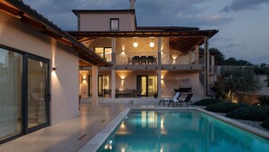 Ein zweistöckiges Haus mit Swimmingpool, Sitzgelegenheiten im Freien und einer überdachten Terrasse.