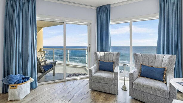 A balcony with a view of the ocean, two armchairs with blue cushions, and a wicker basket on the floor. - Gulf Front Upscale 2BR Condo | Sleeps 6 | 2 Pools | Hot Tub (Pensacola Beach)