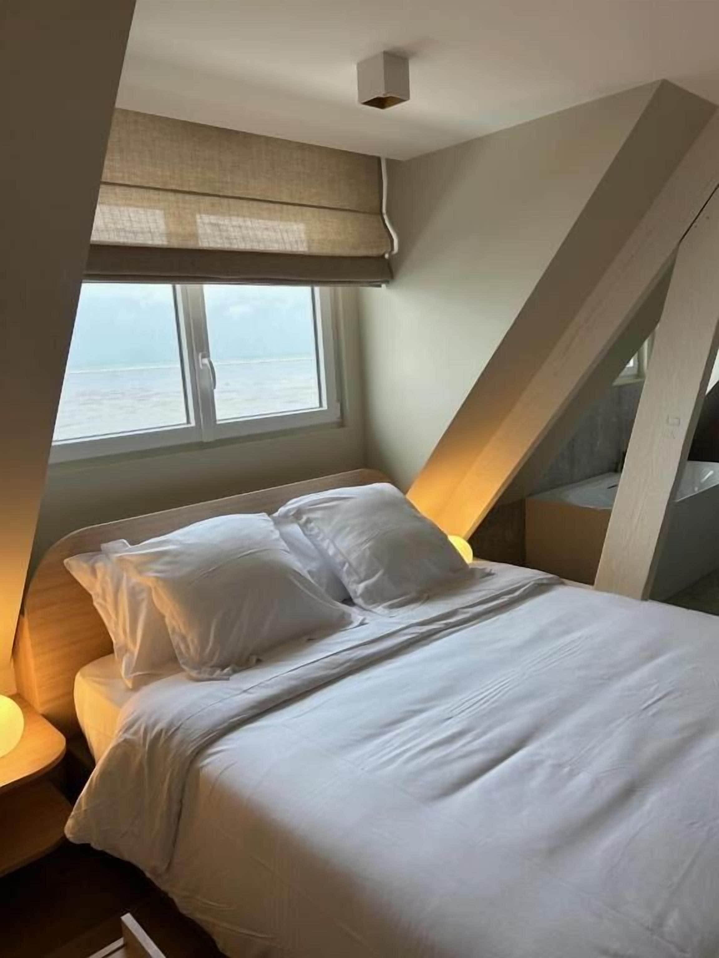 A bedroom with a bed, a window, and a view of the sea.