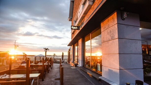 A beachfront restaurant with outdoor seating, a view of the sunset, and a sign indicating the name. - Face à La Mer Gravelines  (Gravelines)