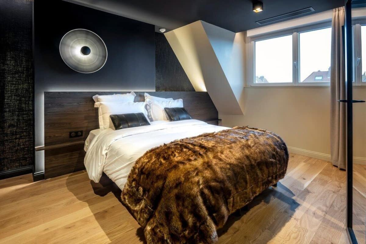 A modern bedroom with a large bed, a unique wall design, and a window with curtains.