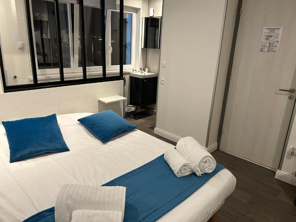 A hotel room with a bed, two pillows, a blue bedspread, and rolled towels.
