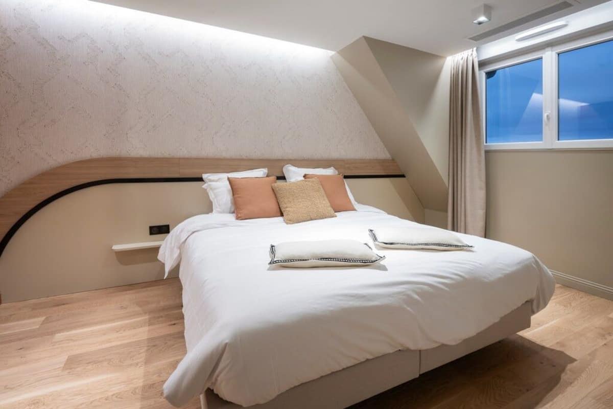 A modern bedroom with a large bed, a headboard, and a window with curtains.