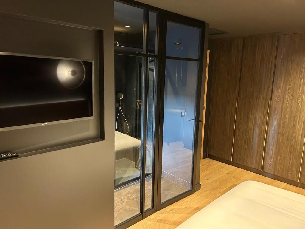 A modern bedroom with a large bed, a built-in TV, and a sliding glass door leading to a bathroom.