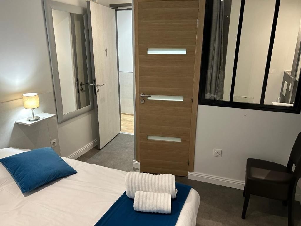 Una habitación de hotel con una cama, una mesita de noche con lámpara, una puerta de madera, un espejo y una silla.