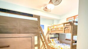 A room with a bunk bed, a wooden ladder, and a desk with drawers.
