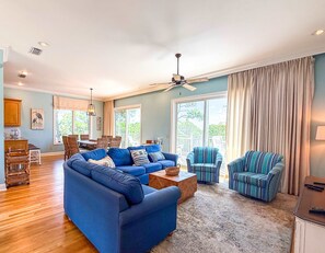 Ein geräumiges Wohnzimmer mit einem blauen Ecksofa, gestreiften Sesseln und einem Deckenventilator.