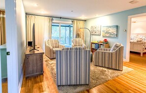 A living room with striped armchairs, a wooden coffee table, and a television on a stand.