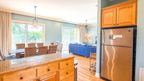 A kitchen with wooden cabinets, a stainless steel refrigerator, and a dining area with wicker furniture.