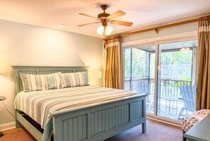 Un dormitorio con cama, ventilador de techo, ventana con cortinas y vistas al exterior.