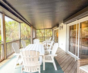 Un espacio al aire libre techado con una terraza de madera, sillas Adirondack blancas y una mesa.