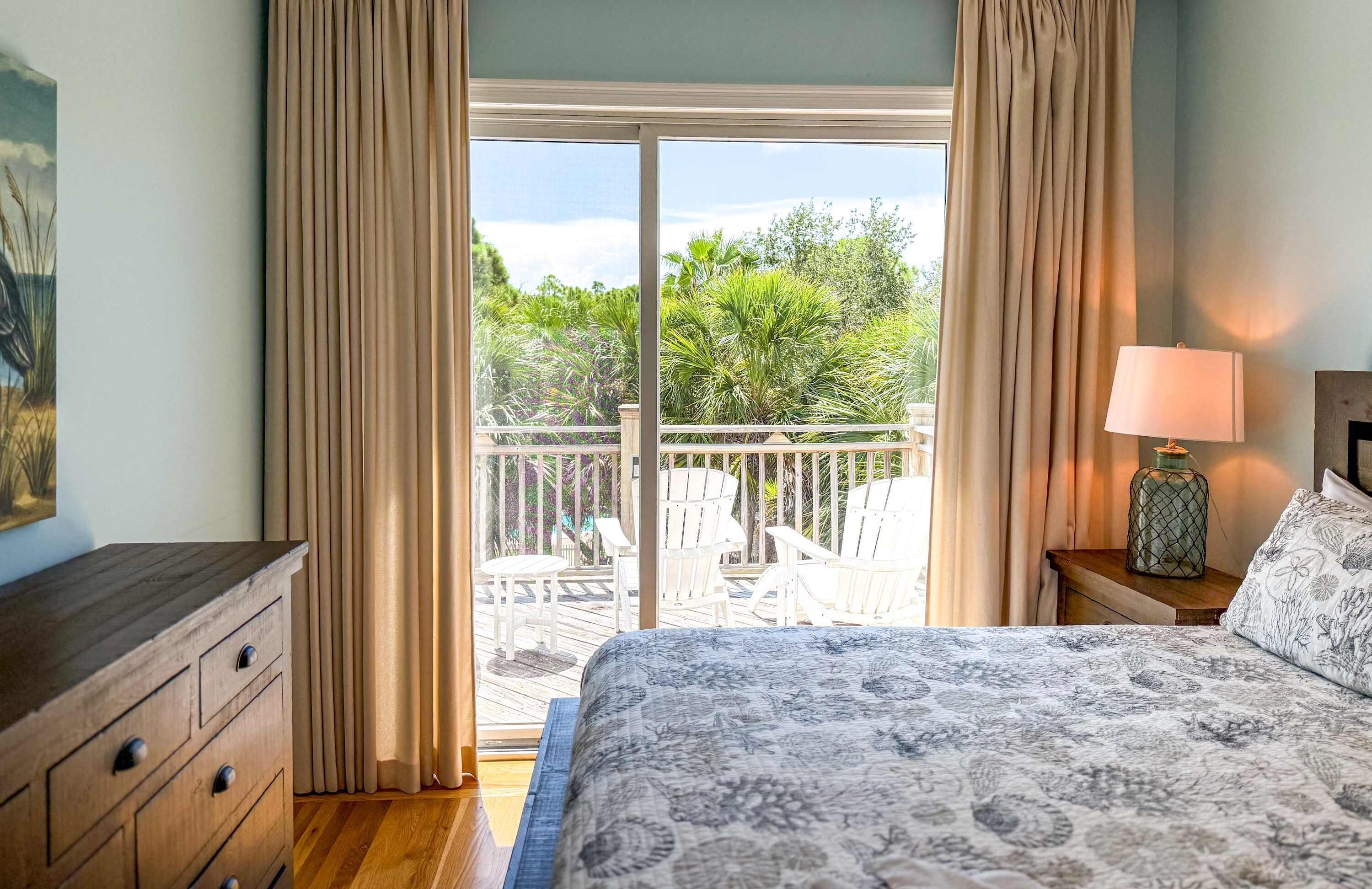 Un dormitorio con una cama grande, una mesita de noche con lámpara y vistas a un balcón con mobiliario exterior.