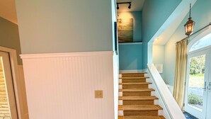 A staircase with a white baseboard, carpeted steps, and a light fixture above.