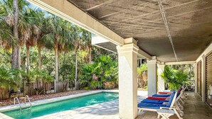 A covered pool area with a clear pool, surrounded by palm trees and a wooden fence.