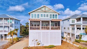 Ein zweistöckiges Strandhaus mit Balkon, überdachter Veranda und Garage.
