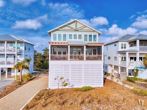 A two-story beachfront house with a balcony, a covered porch, and a garage.