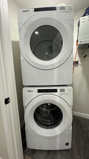 Deux machines à laver Whirlpool superposées dans une buanderie, avec une porte et un appareil fixé au mur.
