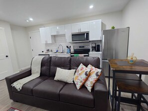 A modern living room with a brown leather sofa, a dining table with chairs, and a kitchen area with white cabinets and appliances. - Cozy 1-bedroom apartment in Regina (Regina)