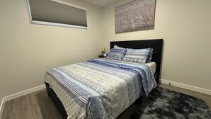 Une chambre à coucher avec un lit, une table de chevet, une lampe, une fenêtre avec des stores et un tableau au mur.