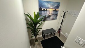 Un couloir avec un pot de fleurs, un banc, un porte-manteau et un tableau représentant un coucher de soleil sur l’océan.