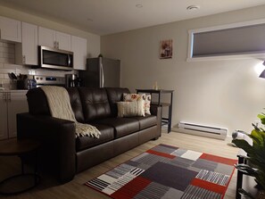 A modern living room with a leather sofa, a coffee table, a patterned rug, and a kitchen in the background.