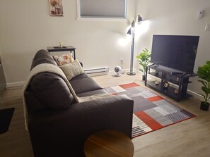 A living room with a sofa, a flat-screen TV, a floor lamp, and a radiator. - Cozy 1-bedroom apartment in Regina (Regina)